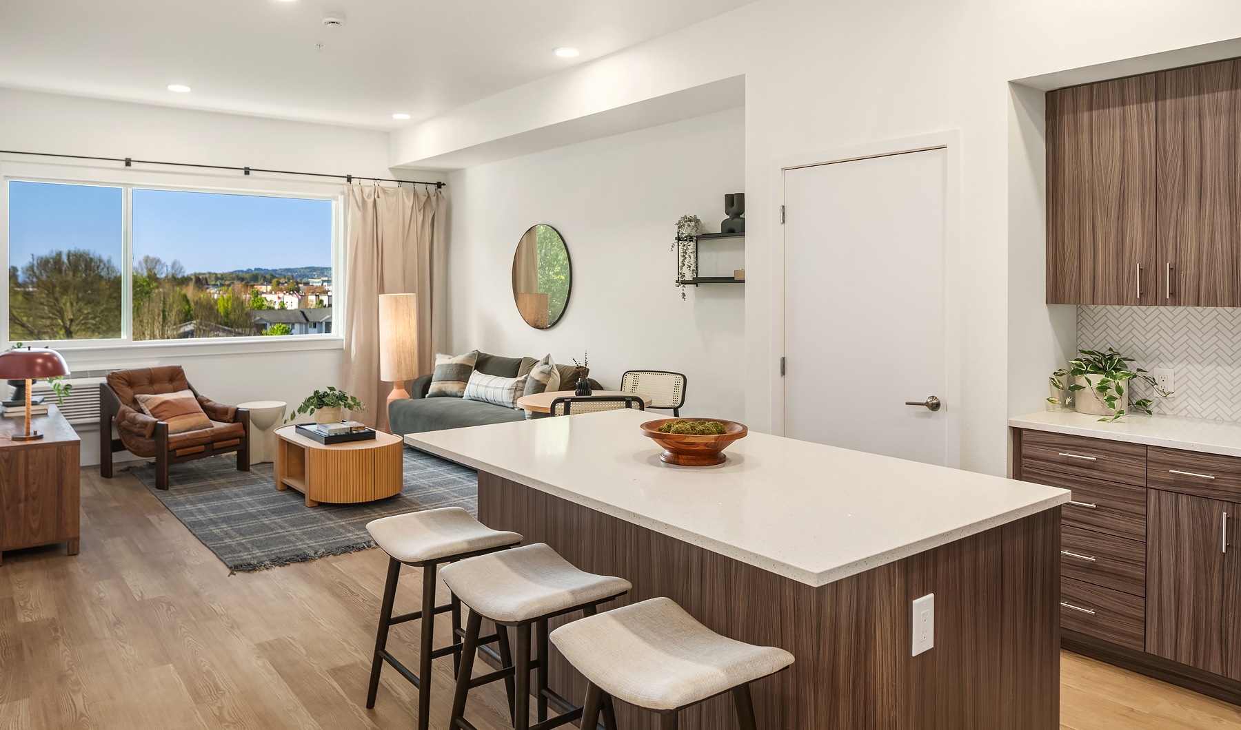 Model living room at our apartments for rent in Kent, WA, featuring wood grain floor paneling and a kitchen island.