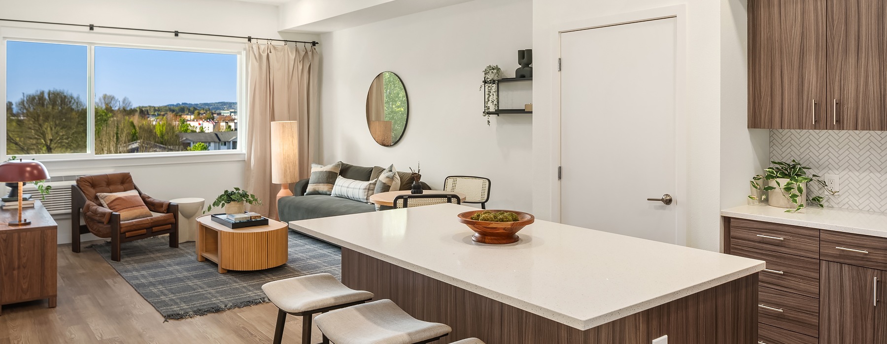 Model living room at our apartments for rent in Kent, WA, featuring wood grain floor paneling and a kitchen island.